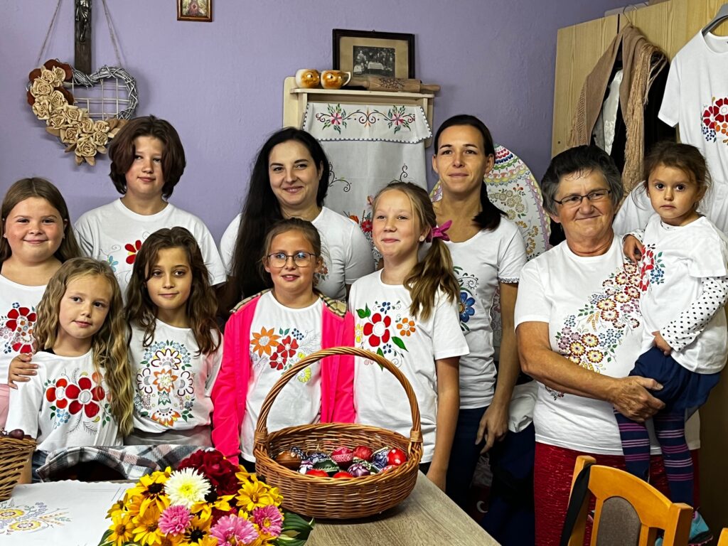 Grupa dzieci z trczynia ludowa po warsztatach, wszyscy maja na sobie białe koszulki wymalowane w kolorowe kwiaty wzoru opolskiego