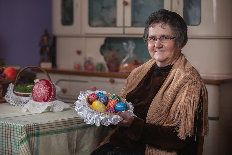 kobieta ubrana w strój ludowy trzyma koszyk z kolorowymi jajkami