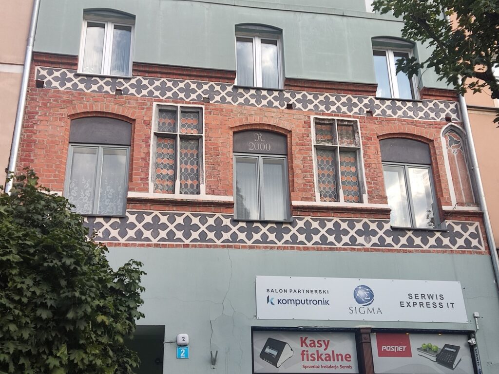 fasada kamienicy z pasem cegieł miedzy gładkim tynkiem