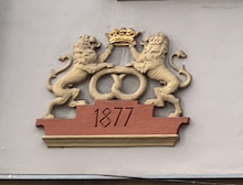 motyw precla z kamienicy przy ul Chopina 1 w Brzegu sztukateria na kamienicy: dwa lwy trzymające koronę, pomiędzy nimi precel. Lwy stoją na podeście z napisem 1877