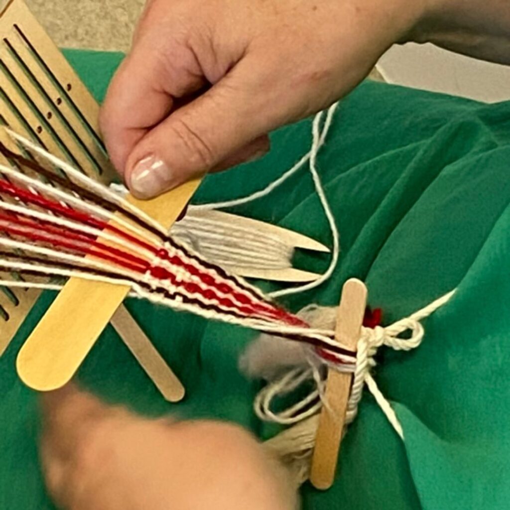 dłoń trzyma patyk, przepleciony przez tworzącą się krajkę