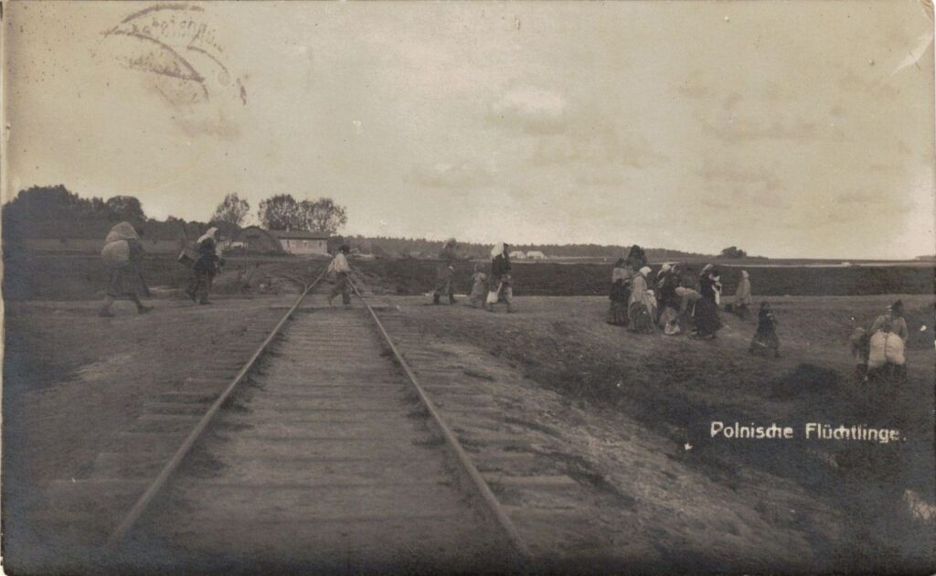 Stare zdjęcie, czarnobiałe przedstawia sylwetki biednych ludzi idących z tobołkami przez tory